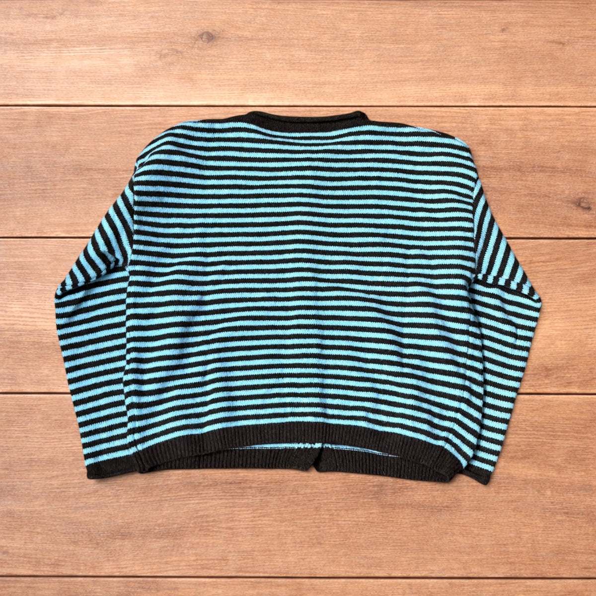 Turquoise and black striped vintage knitted cardigan jumper with button-up front laid flat on wooden surface.