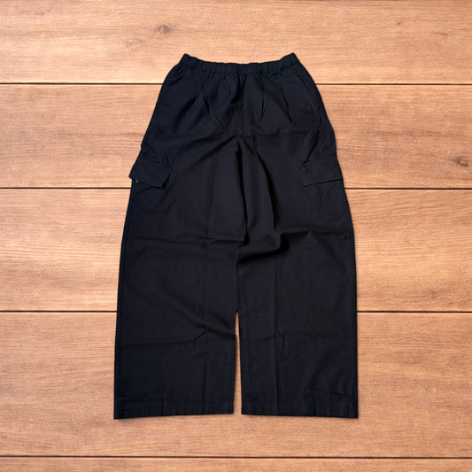 Black baggy wide leg cargo trousers laid flat on wooden surface showing elasticated waistband and cargo pockets.