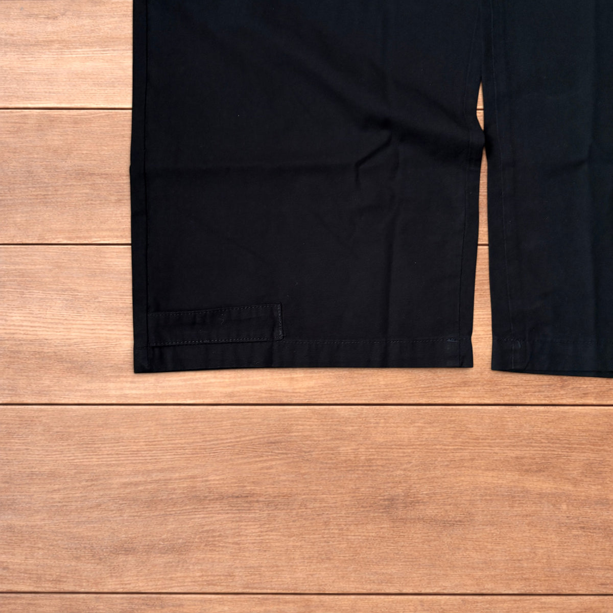Black baggy wide leg cargo trousers laid flat on wooden surface showing elasticated waistband and cargo pockets.