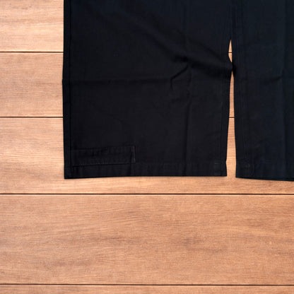 Black baggy wide leg cargo trousers laid flat on wooden surface showing elasticated waistband and cargo pockets.