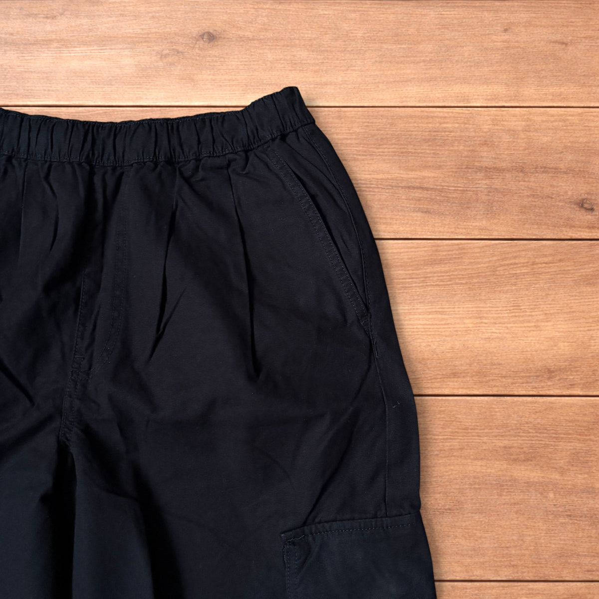 Black baggy wide leg cargo trousers laid flat on wooden surface showing elasticated waistband and cargo pockets.