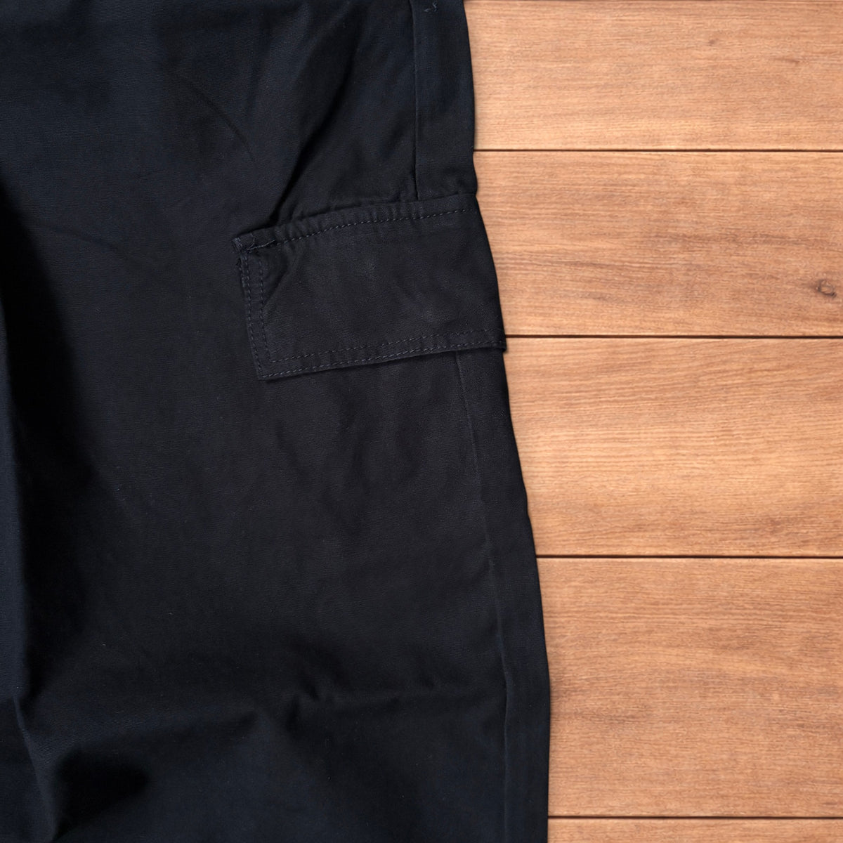 Black baggy wide leg cargo trousers laid flat on wooden surface showing elasticated waistband and cargo pockets.