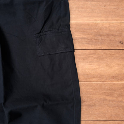Black baggy wide leg cargo trousers laid flat on wooden surface showing elasticated waistband and cargo pockets.