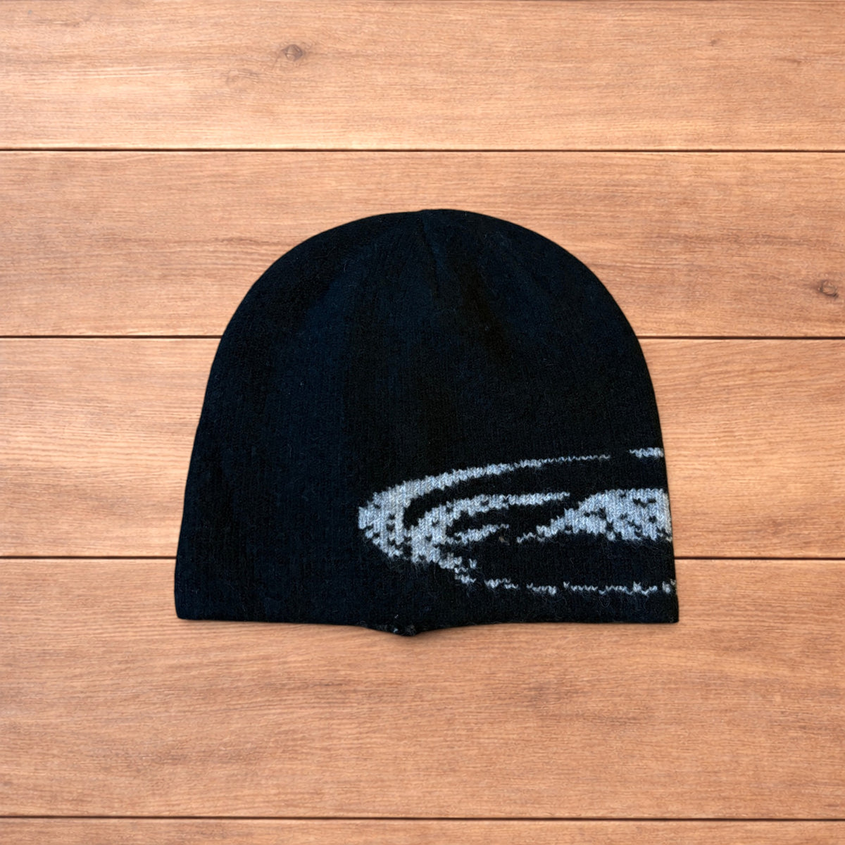 Black Japanese style graphic beanie with grey pattern and reversible inside, laid flat on wood background