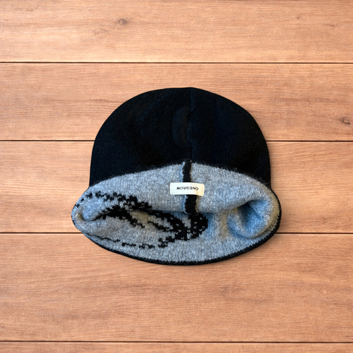 Black Japanese style graphic beanie with grey pattern and reversible inside, laid flat on wood background