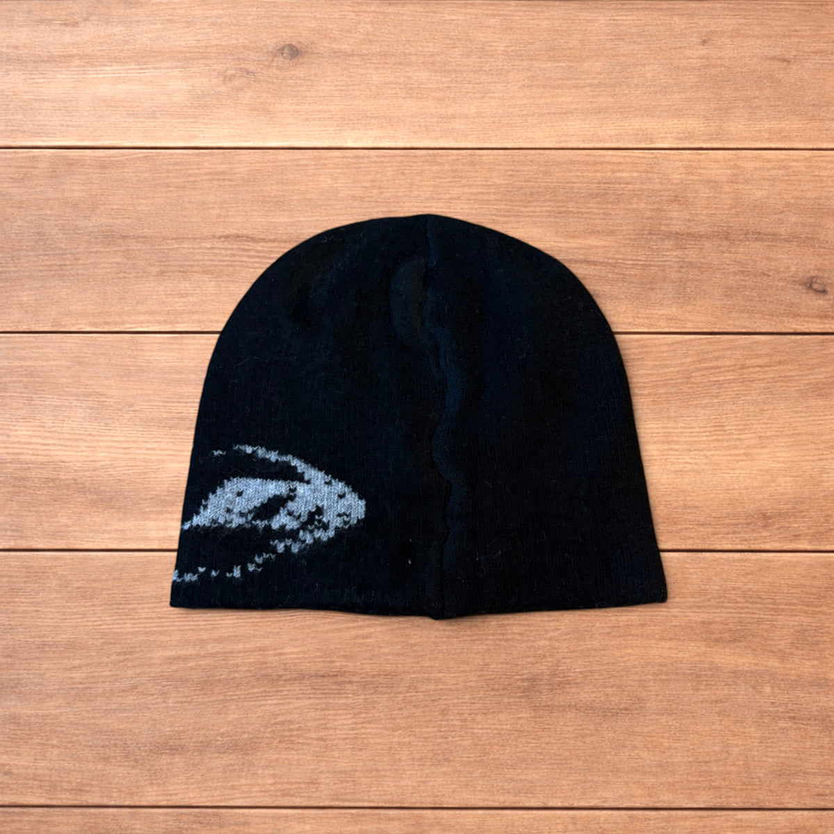 Black Japanese style graphic beanie with grey pattern and reversible inside, laid flat on wood background