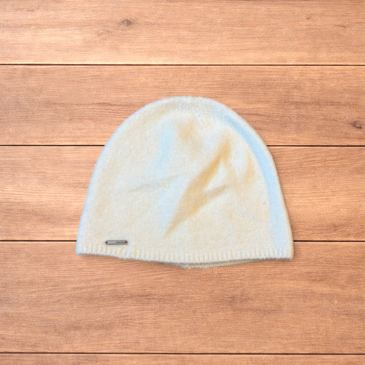 Pastel brown Korean style knitted beanie with sewn on metal tag detail on wooden surface.