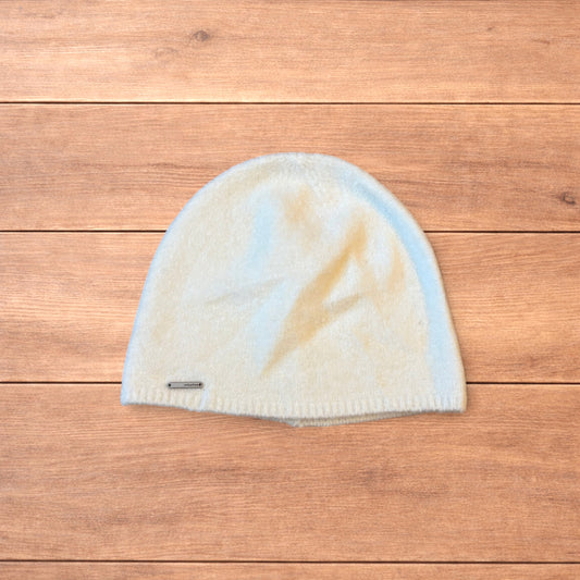 Pastel brown Korean style knitted beanie with sewn on metal tag detail on wooden surface.