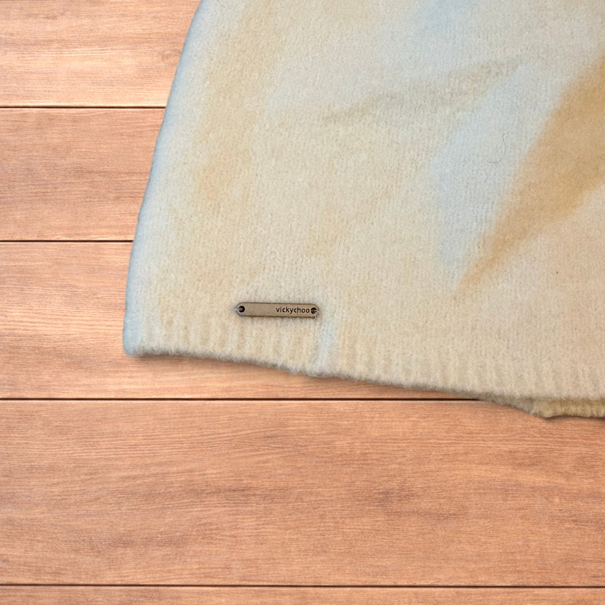 Pastel brown Korean style knitted beanie with sewn on metal tag detail on wooden surface.