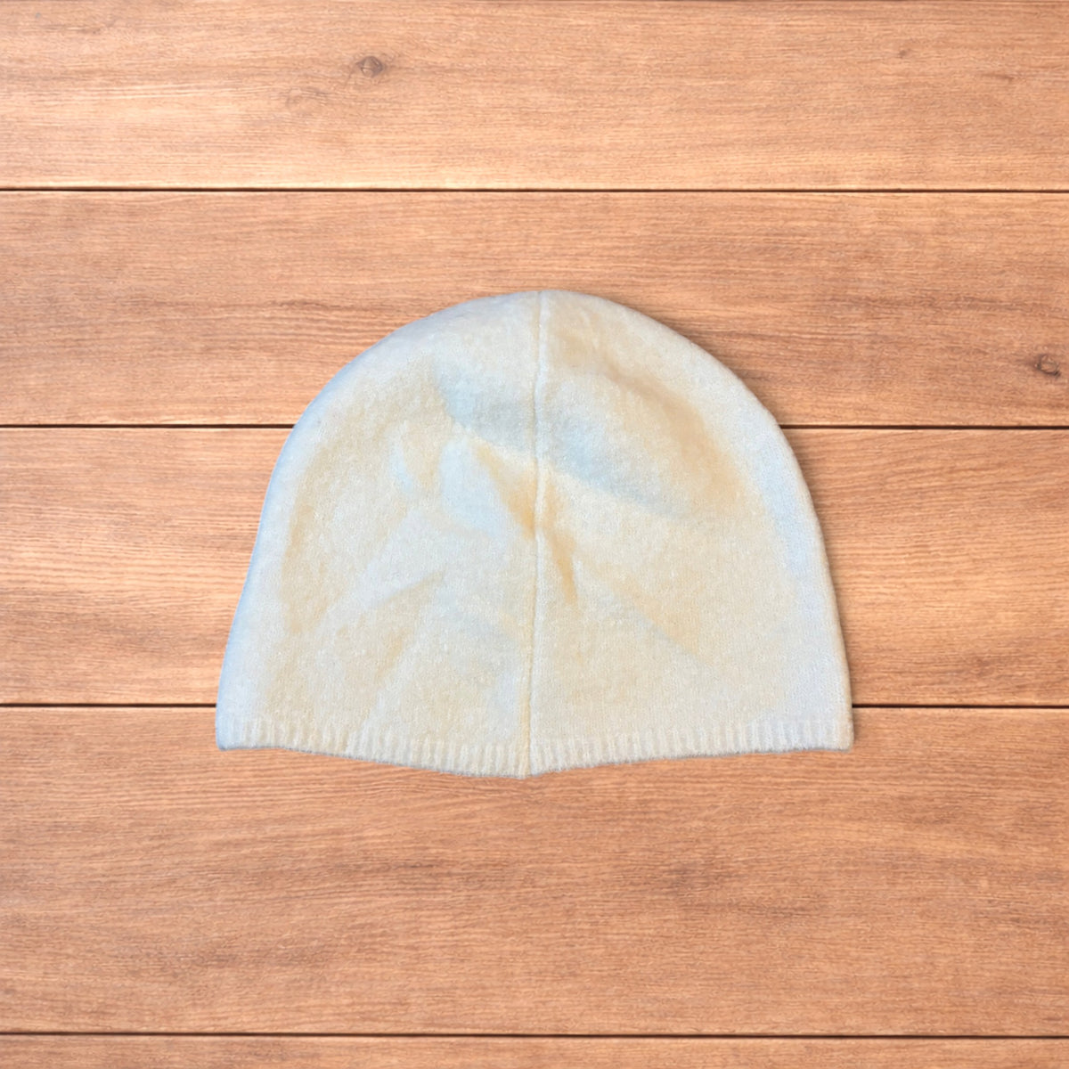 Pastel brown Korean style knitted beanie with sewn on metal tag detail on wooden surface.