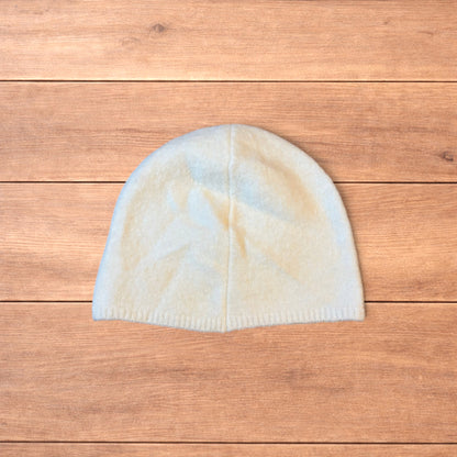Pastel brown Korean style knitted beanie with sewn on metal tag detail on wooden surface.