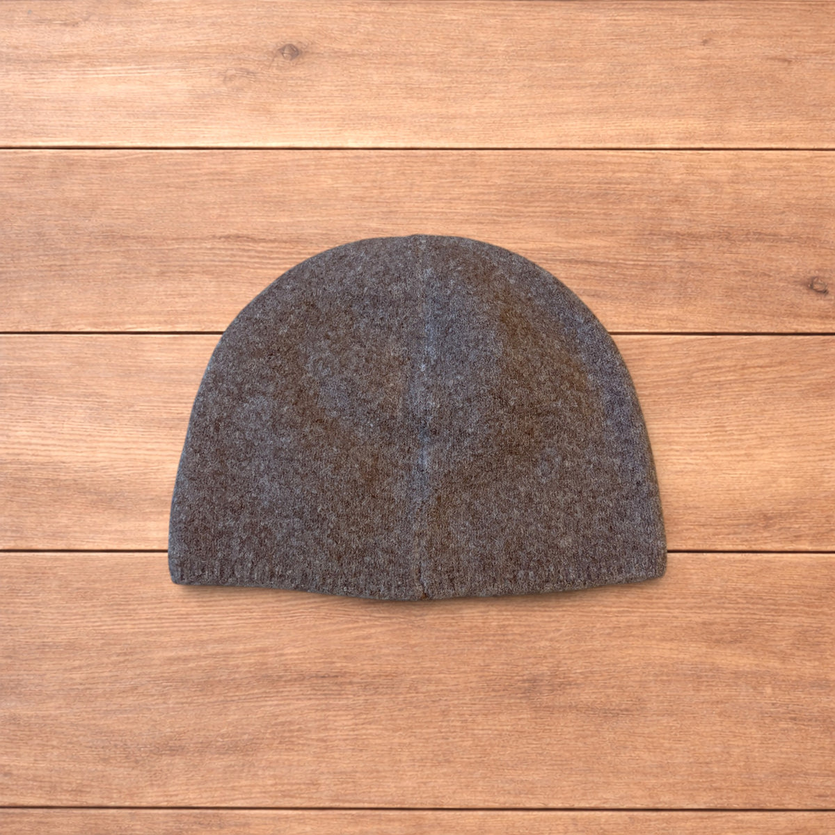 Pastel brown Korean style knitted beanie with sewn-on metal logo detail on wooden background.