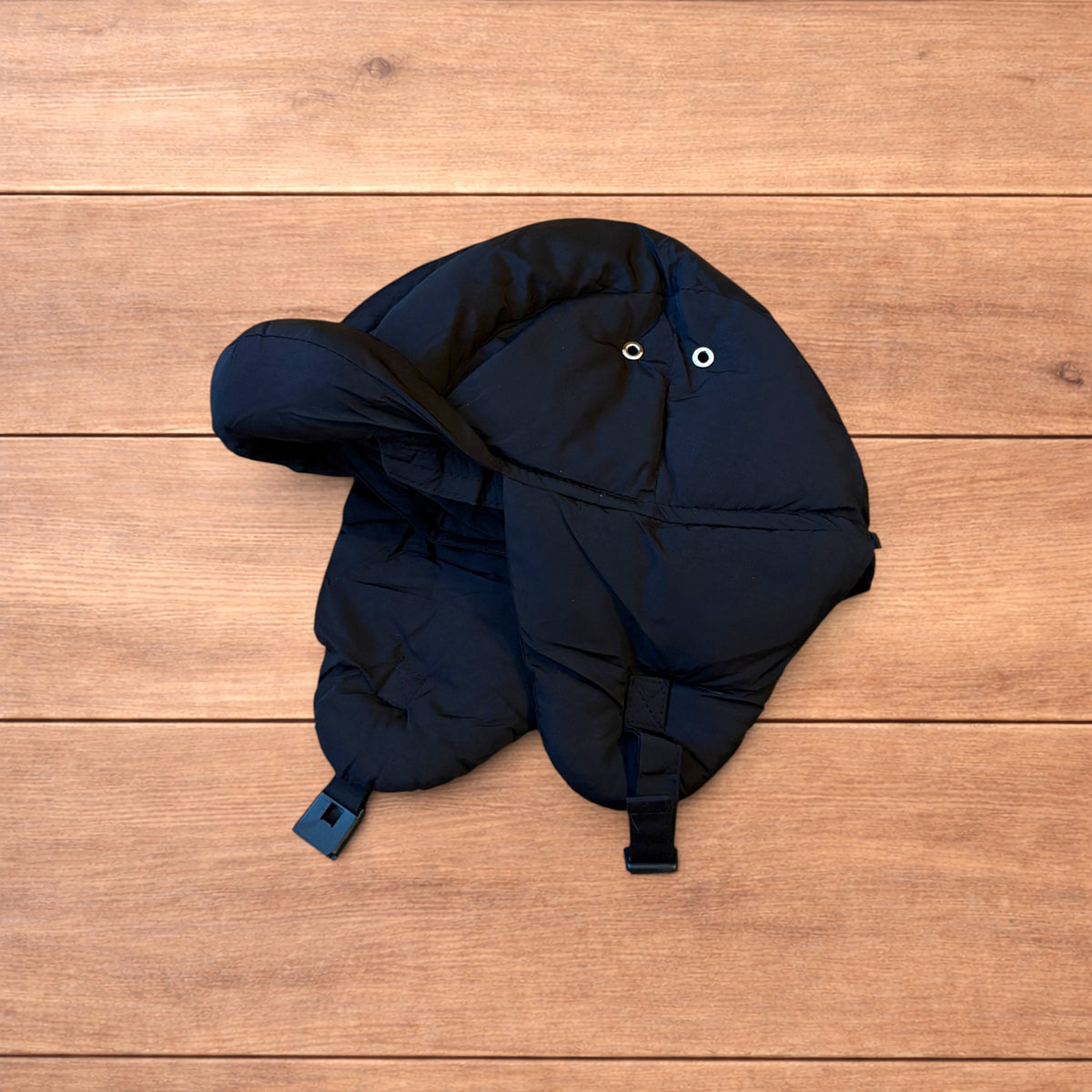 Black Korean style puffer padded trapper hat with ear flaps and metal air vents on wooden surface.