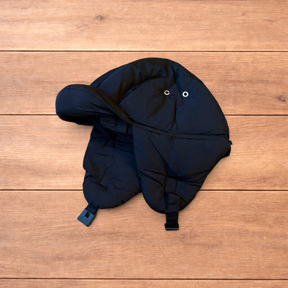 Black Korean style puffer padded trapper hat with ear flaps and metal air vents on wooden surface.