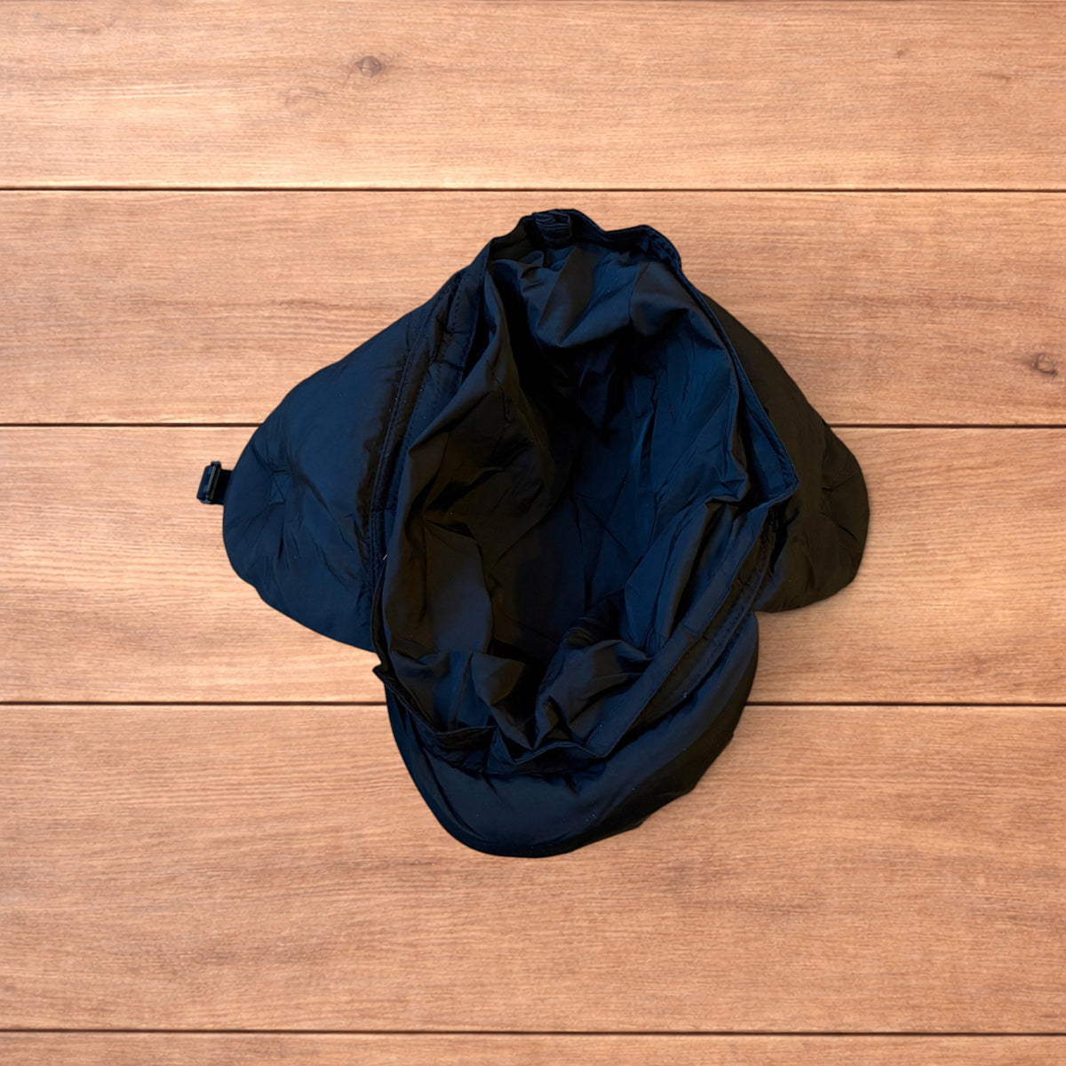 Black Korean style puffer padded trapper hat with ear flaps and metal air vents on wooden surface.