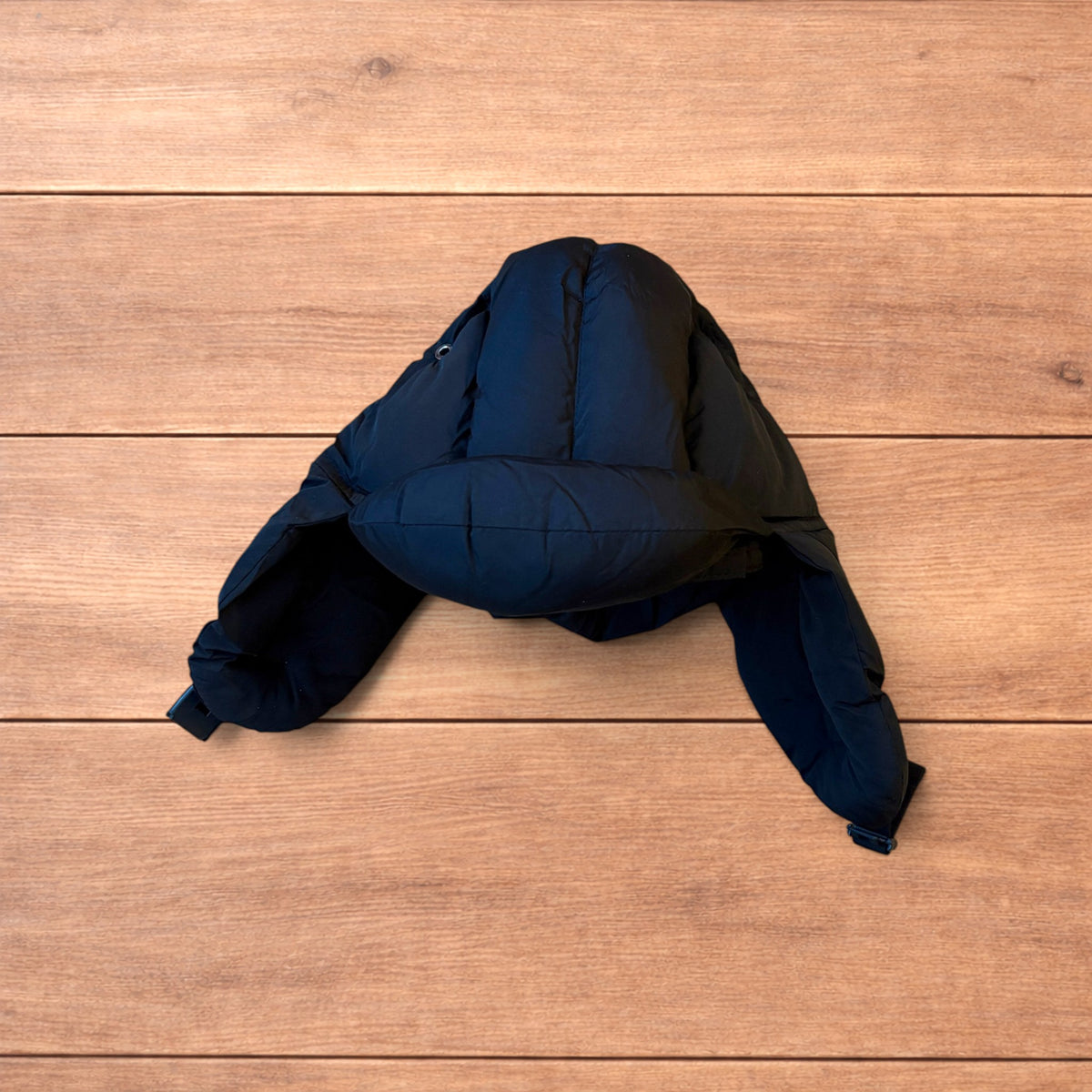 Black Korean style puffer padded trapper hat with ear flaps and metal air vents on wooden surface.