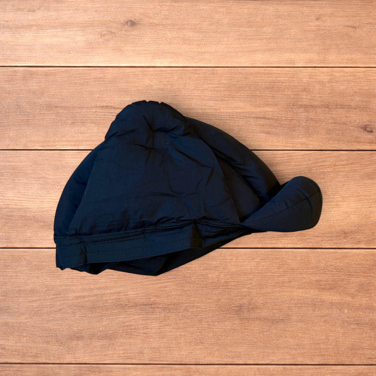 Black Korean style puffer padded trapper hat with ear flaps and metal air vents on wooden surface.