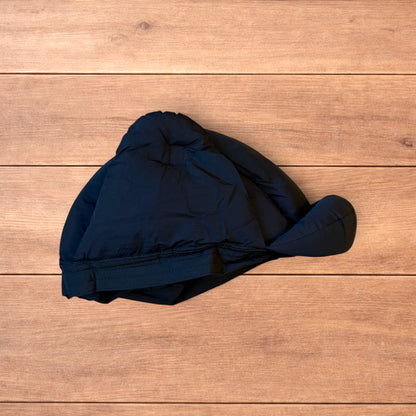 Black Korean style puffer padded trapper hat with ear flaps and metal air vents on wooden surface.