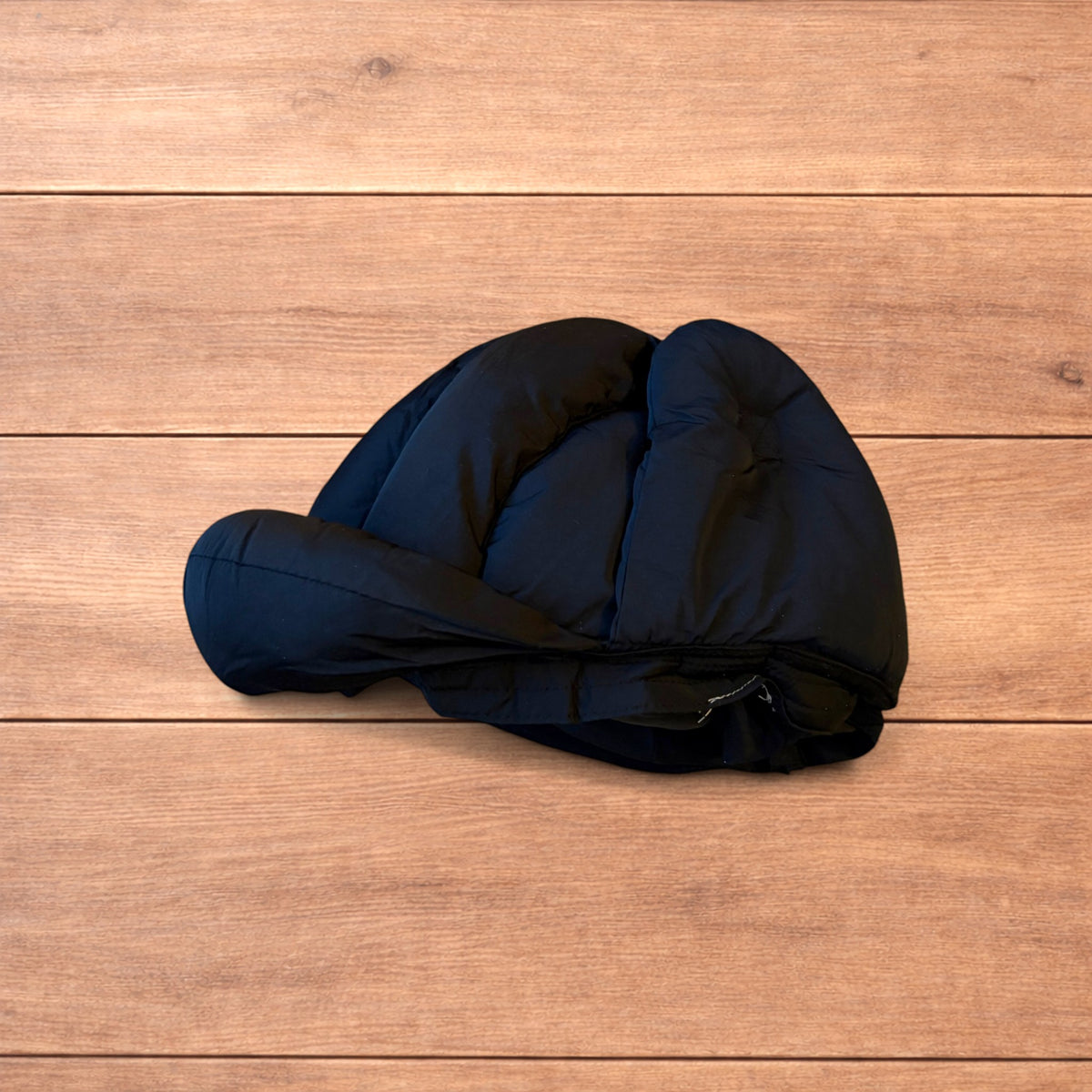 Black Korean style puffer padded trapper hat with ear flaps and metal air vents on wooden surface.