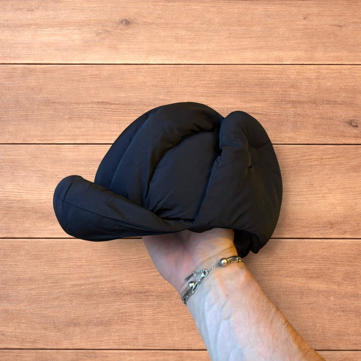 Black Korean style puffer padded trapper hat with ear flaps and metal air vents on wooden surface.