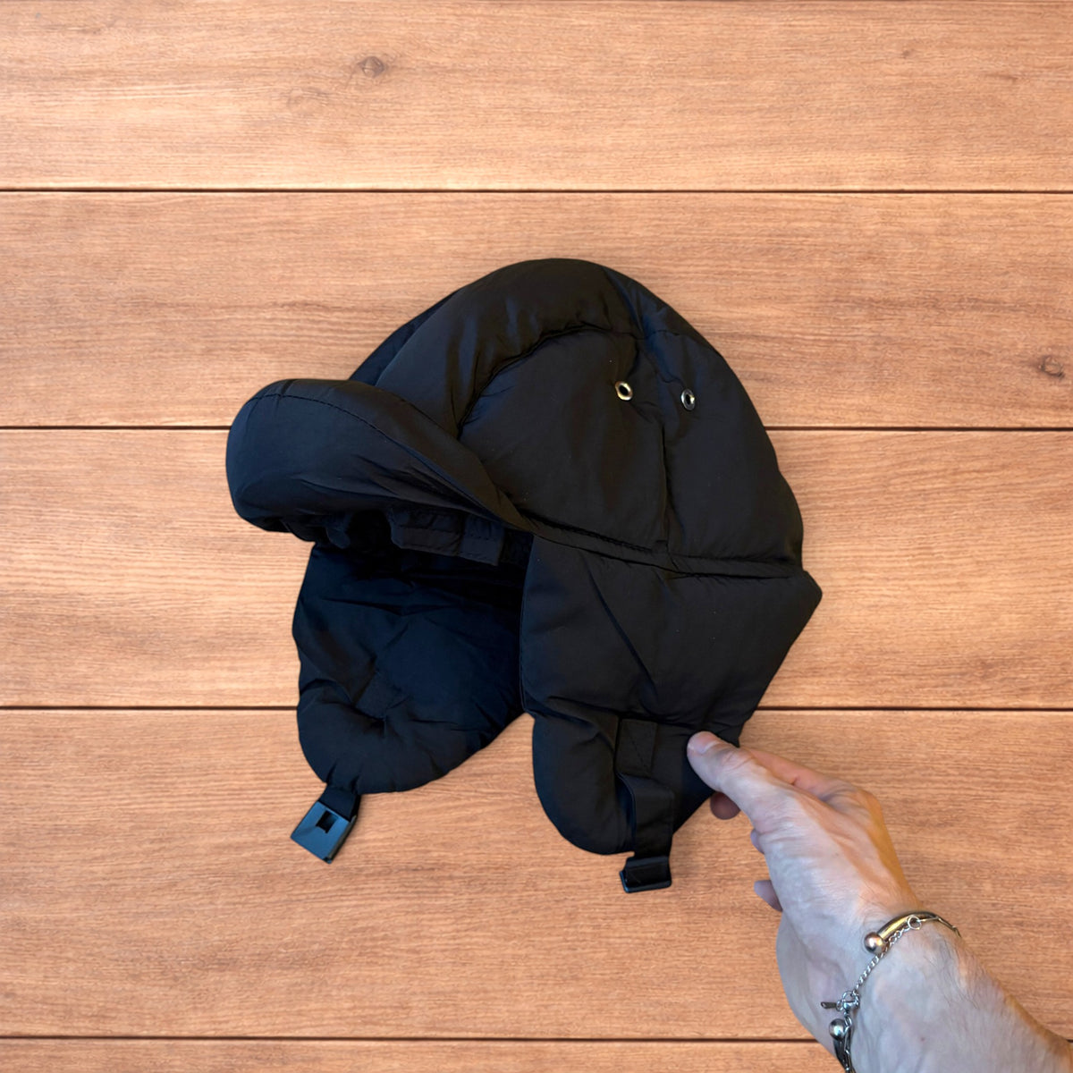 Black Korean style puffer padded trapper hat with ear flaps and metal air vents on wooden surface.