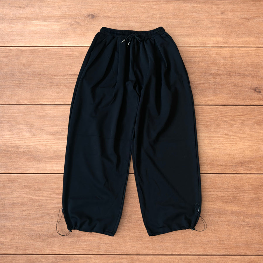Korean black baggy wide leg joggers laid flat on wooden background showing front, back, and adjustable features.