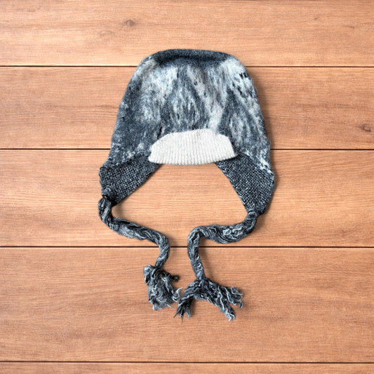 Korean style dappy ear flap hat in grey and cream with braided ties on wooden background.