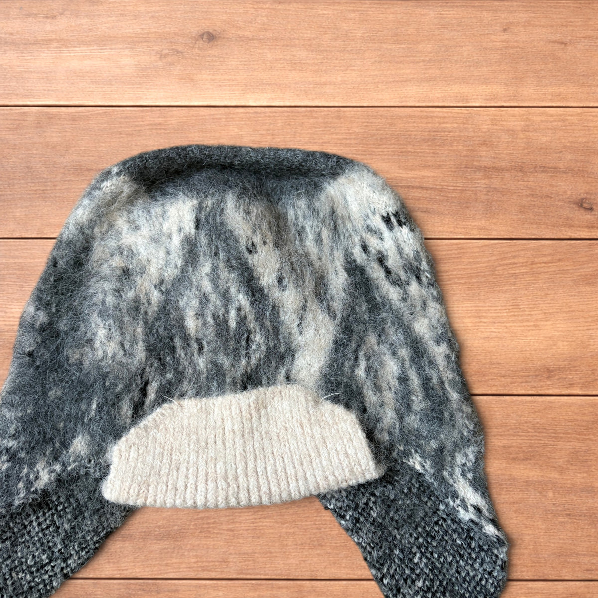 Korean style dappy ear flap hat in grey and cream with braided ties on wooden background.