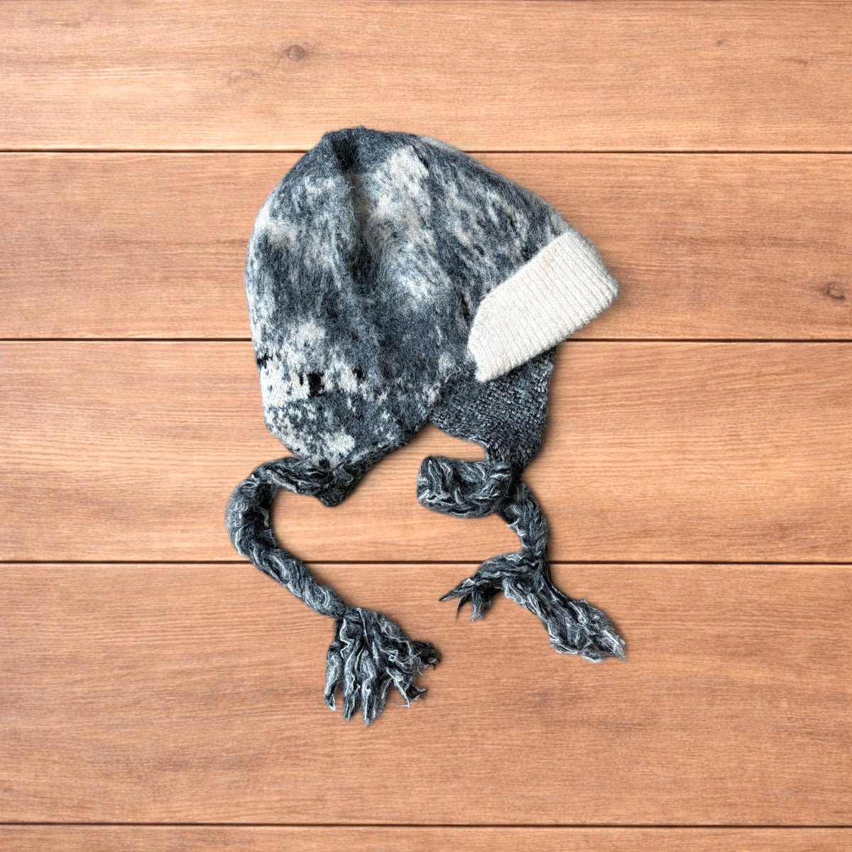 Korean style dappy ear flap hat in grey and cream with braided ties on wooden background.