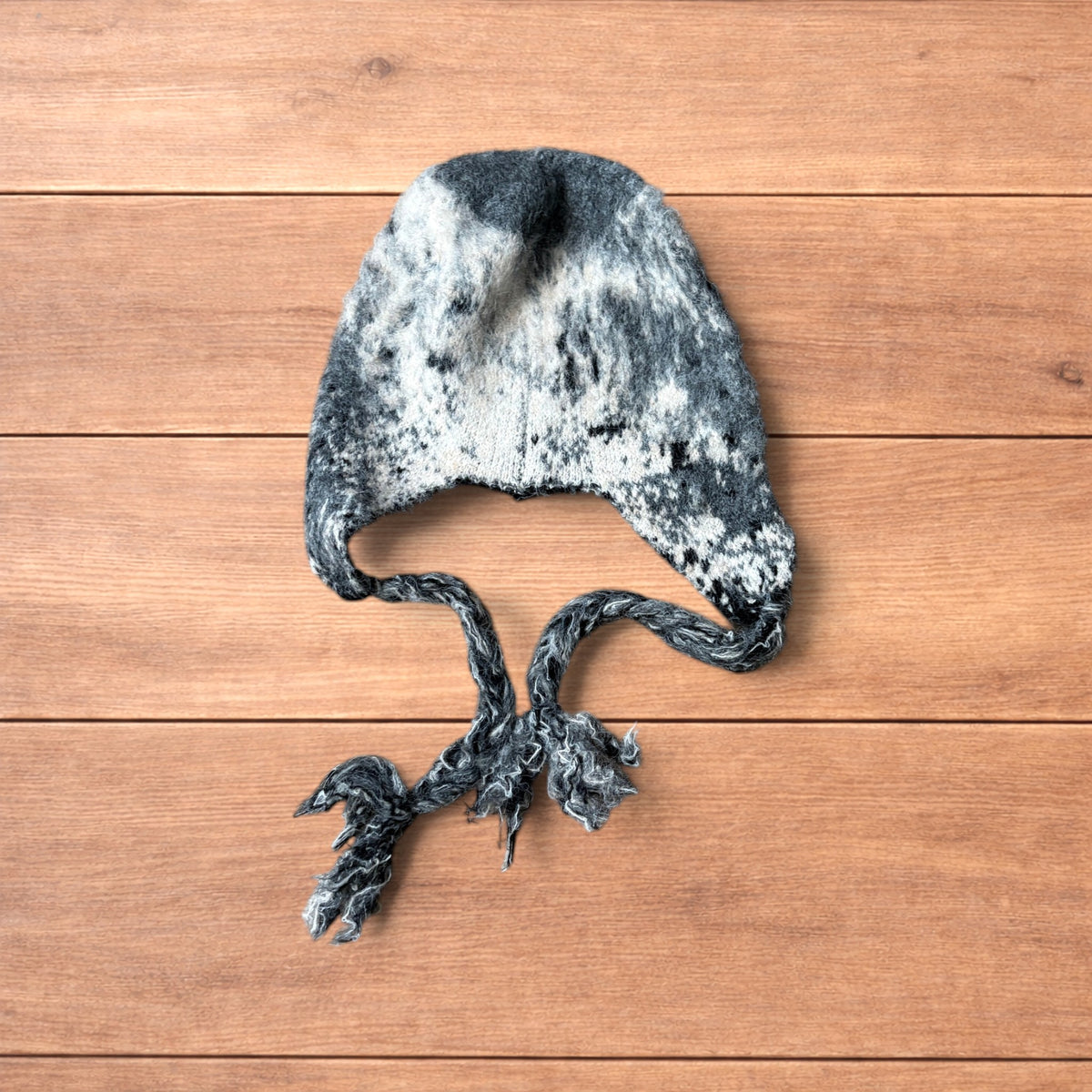 Korean style dappy ear flap hat in grey and cream with braided ties on wooden background.