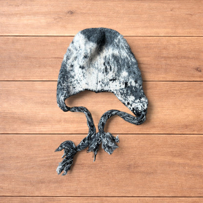 Korean style dappy ear flap hat in grey and cream with braided ties on wooden background.