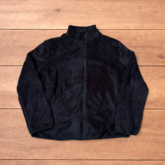 Black fleece fluffy zip up jacket laid flat on wooden floor showing full front, collar, sleeves, and pockets.