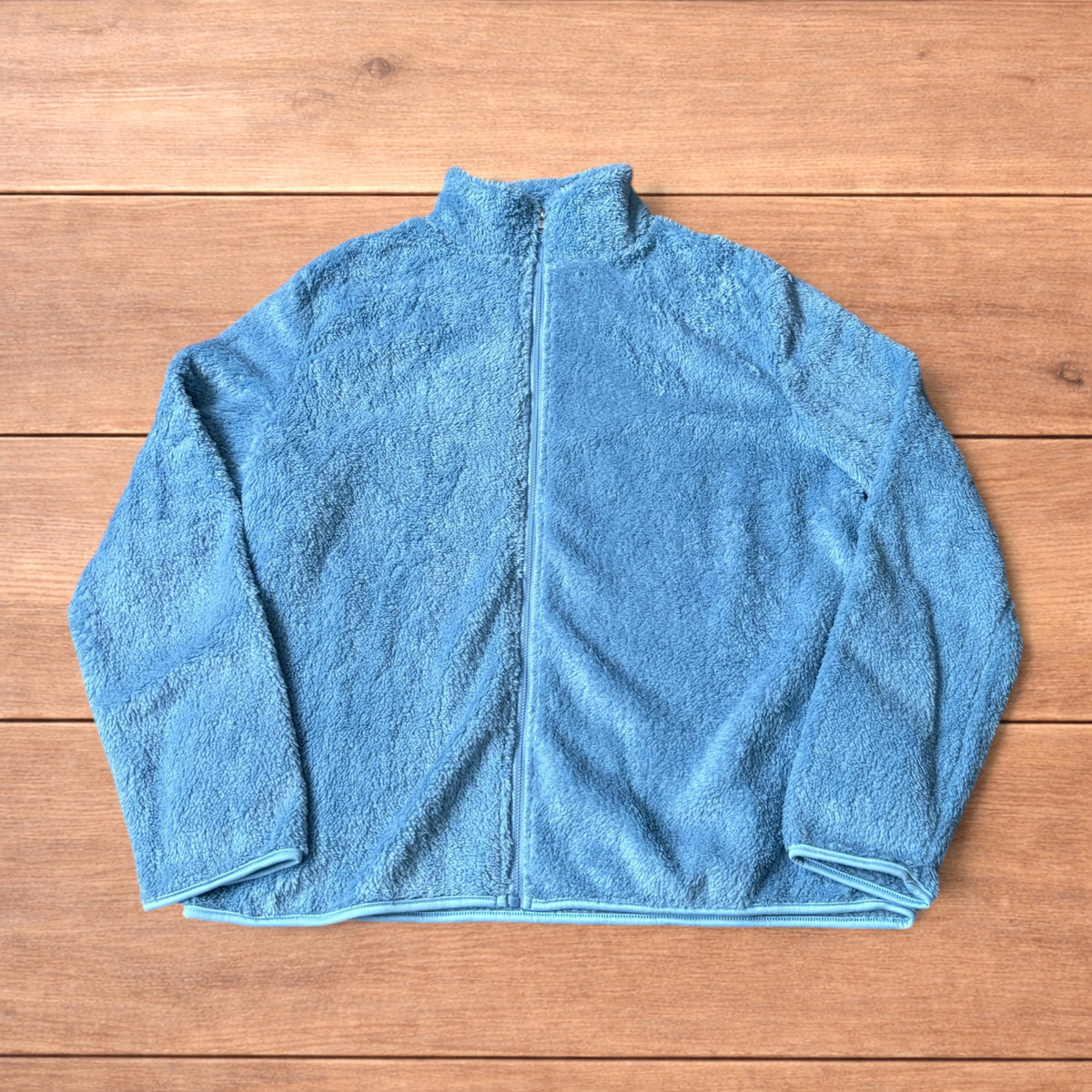 Light blue fleece fluffy zip up jacket laid flat on wooden surface.