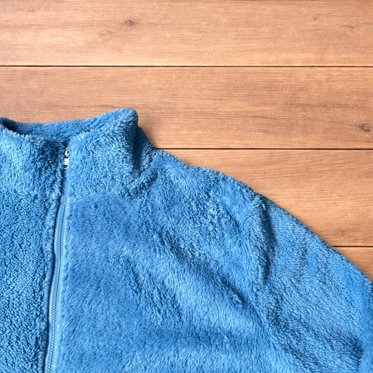 Light blue fleece fluffy zip up jacket laid flat on wooden surface.