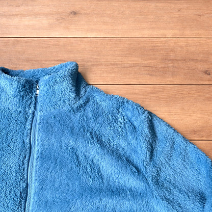 Light blue fleece fluffy zip up jacket laid flat on wooden surface.