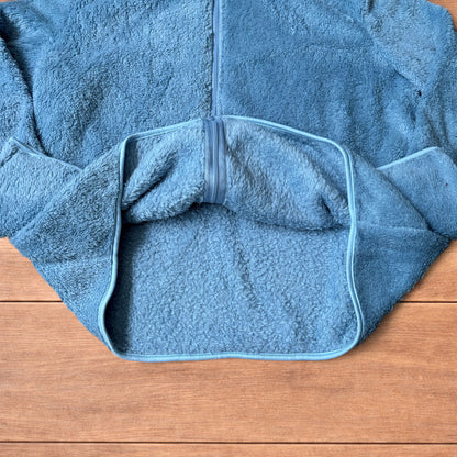 Light blue fleece fluffy zip up jacket laid flat on wooden surface.