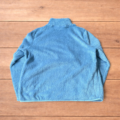 Light blue fleece fluffy zip up jacket laid flat on wooden surface.