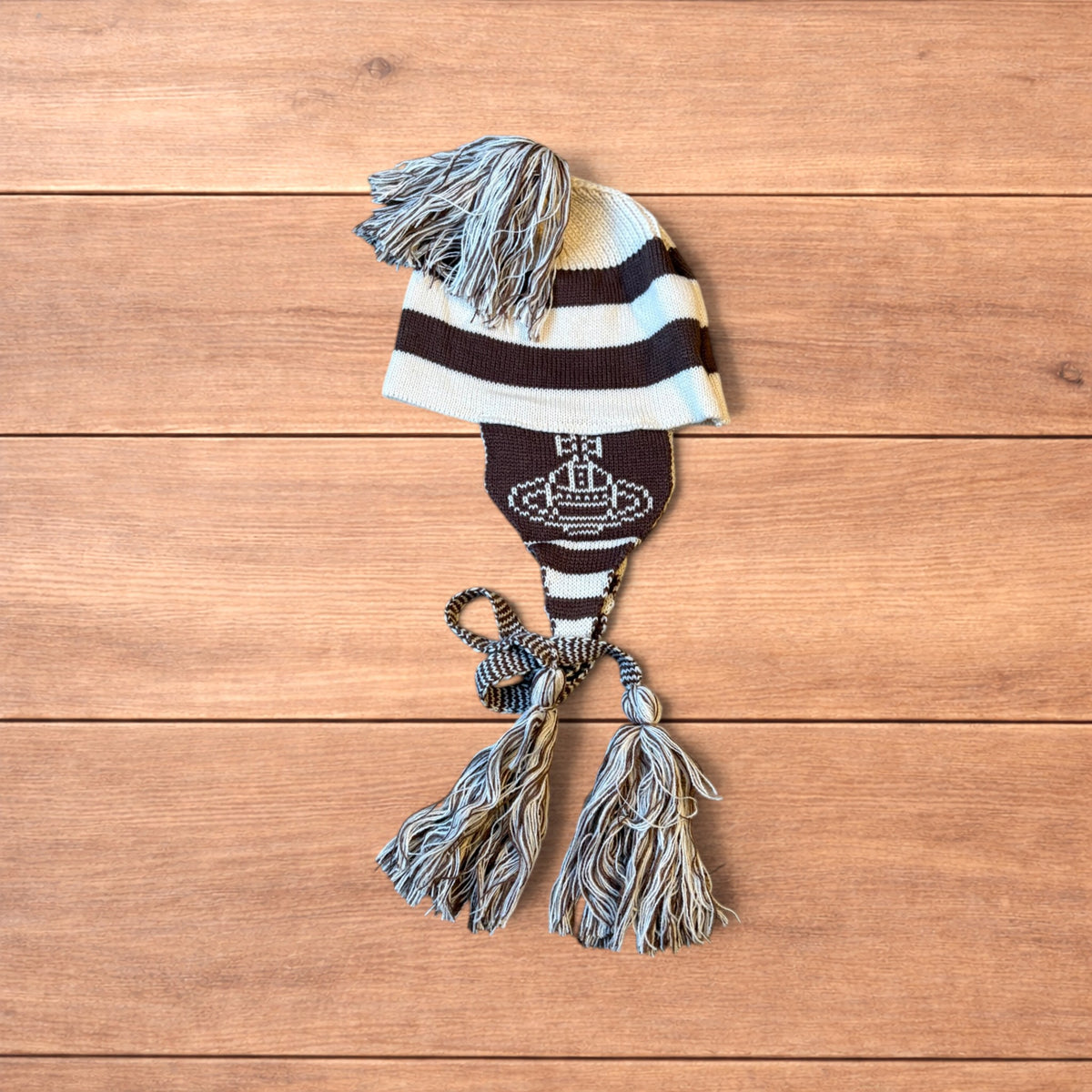 Vintage style striped dappy bobble hat with ear flaps and tassels in brown and cream laid flat on wooden surface.