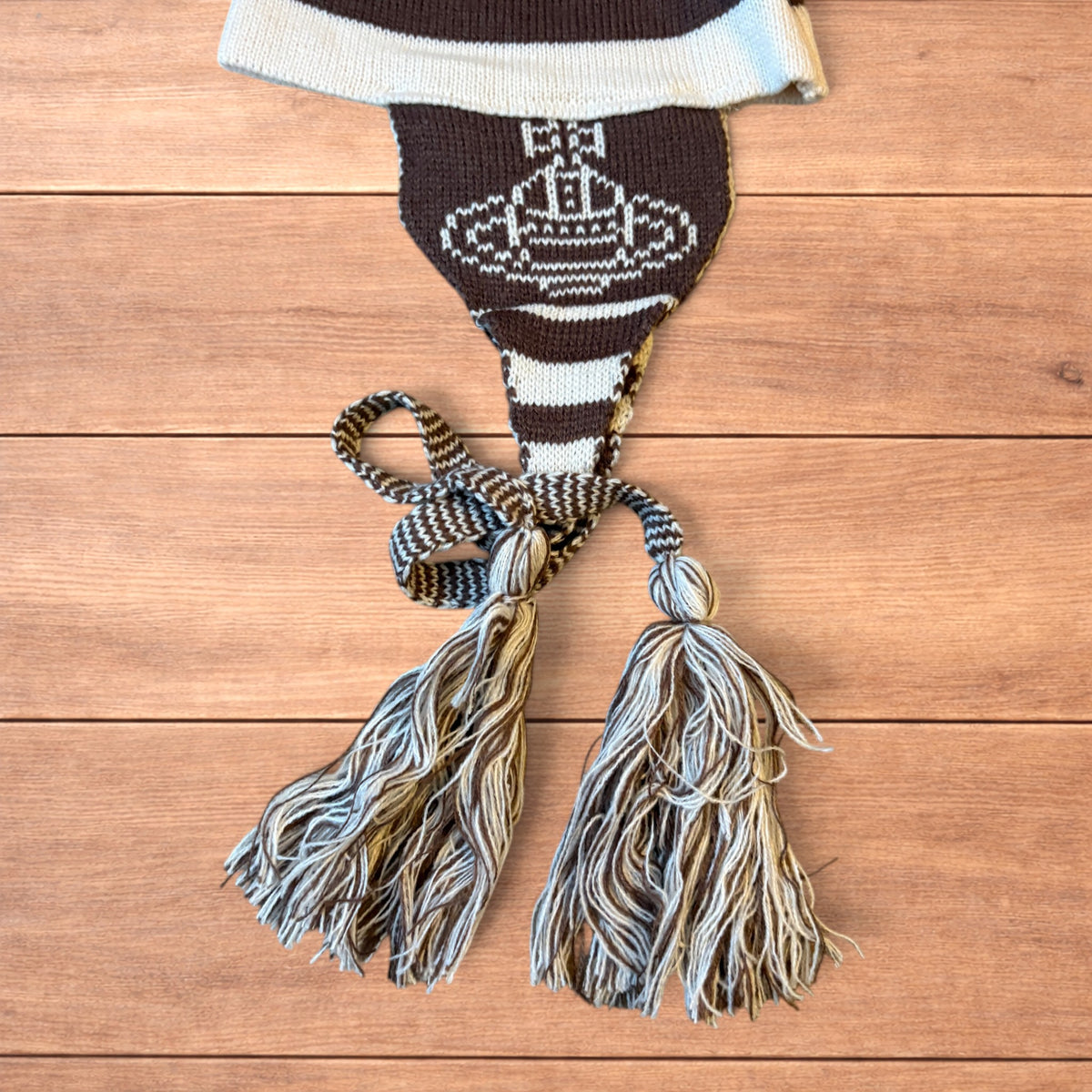Vintage style striped dappy bobble hat with ear flaps and tassels in brown and cream laid flat on wooden surface.