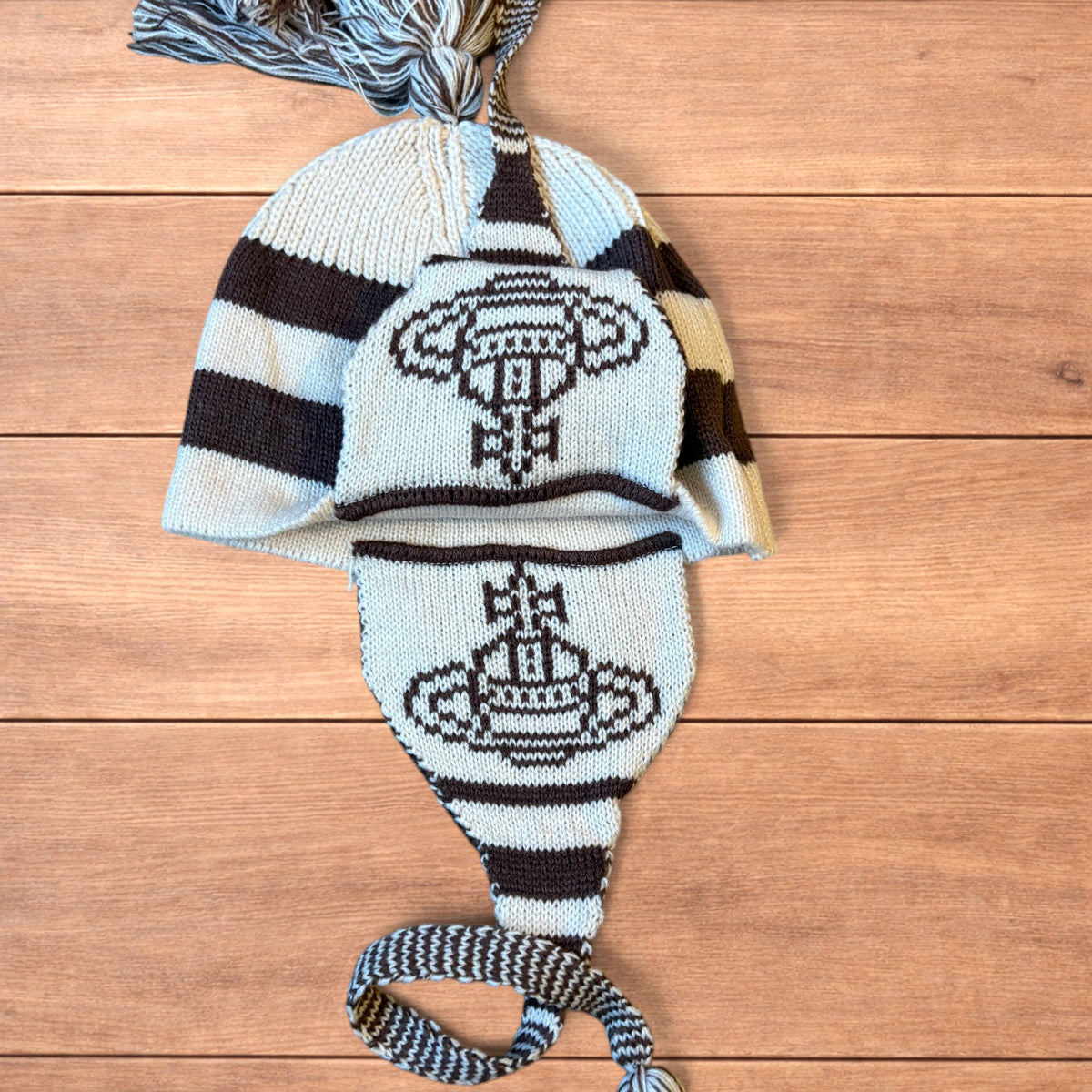 Vintage style striped dappy bobble hat with ear flaps and tassels in brown and cream laid flat on wooden surface.