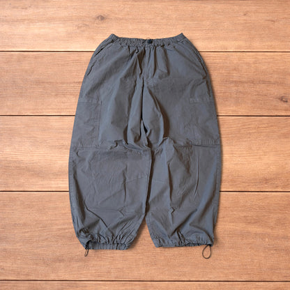 Grey baggy wide leg ripstop cargo trousers with cargo pockets, elasticated waistband and toggled hems laid flat on wooden floor.
