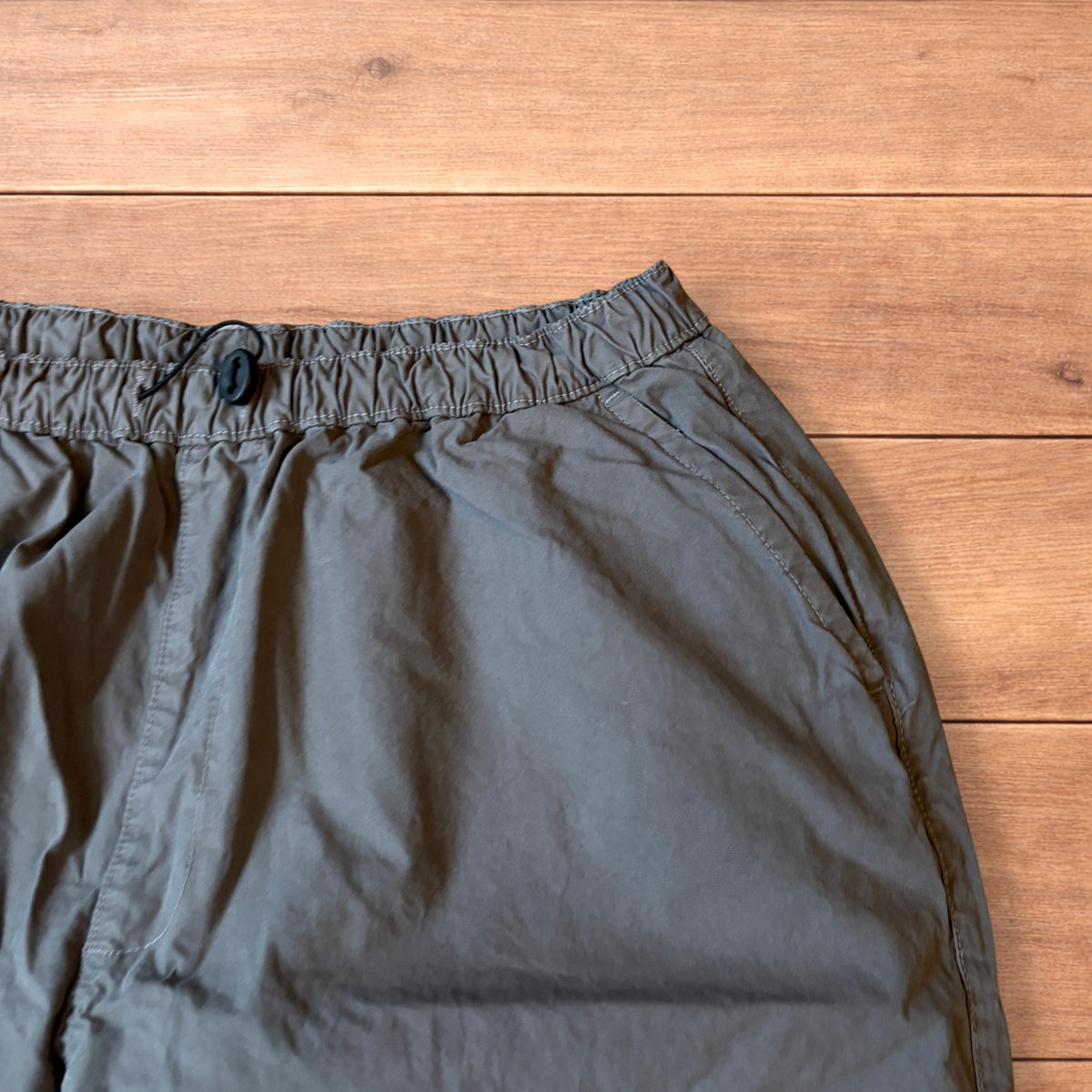 Grey baggy wide leg ripstop cargo trousers with cargo pockets, elasticated waistband and toggled hems laid flat on wooden floor.