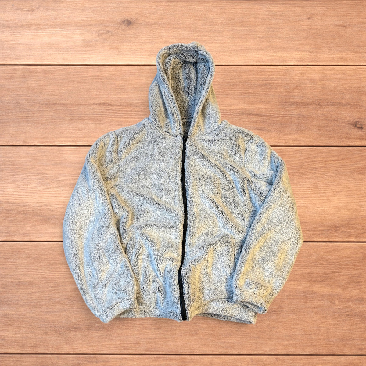 Light grey fluffy zip up hoodie jacket with full zip and hood displayed on wooden floor background