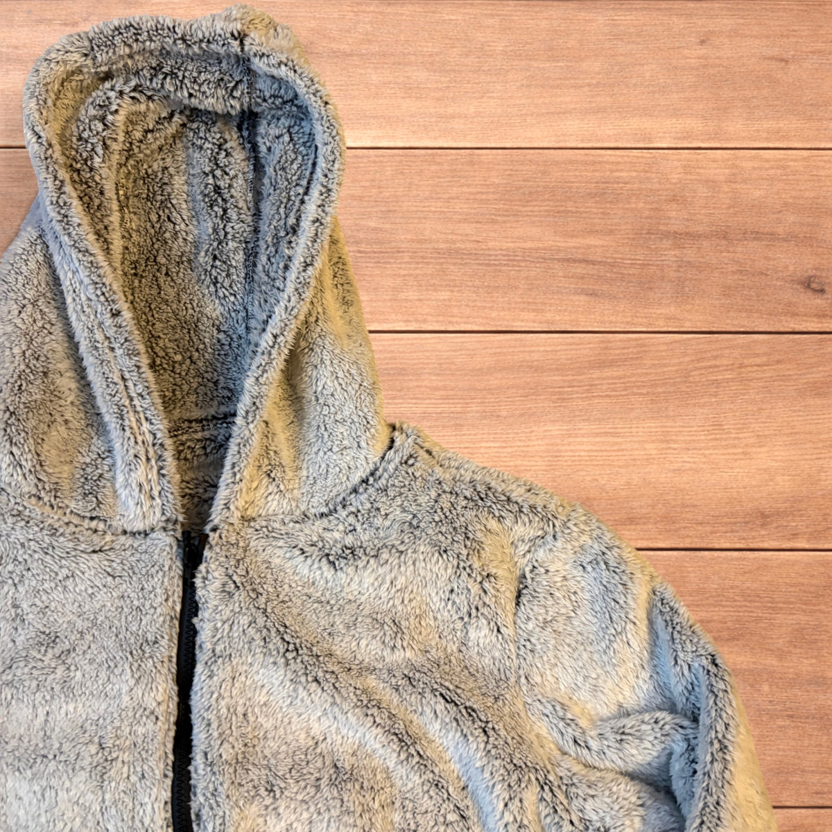 Light grey fluffy zip up hoodie jacket with full zip and hood displayed on wooden floor background