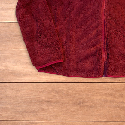 Deep dark red fluffy fleece zip up jacket laid flat on wooden surface.