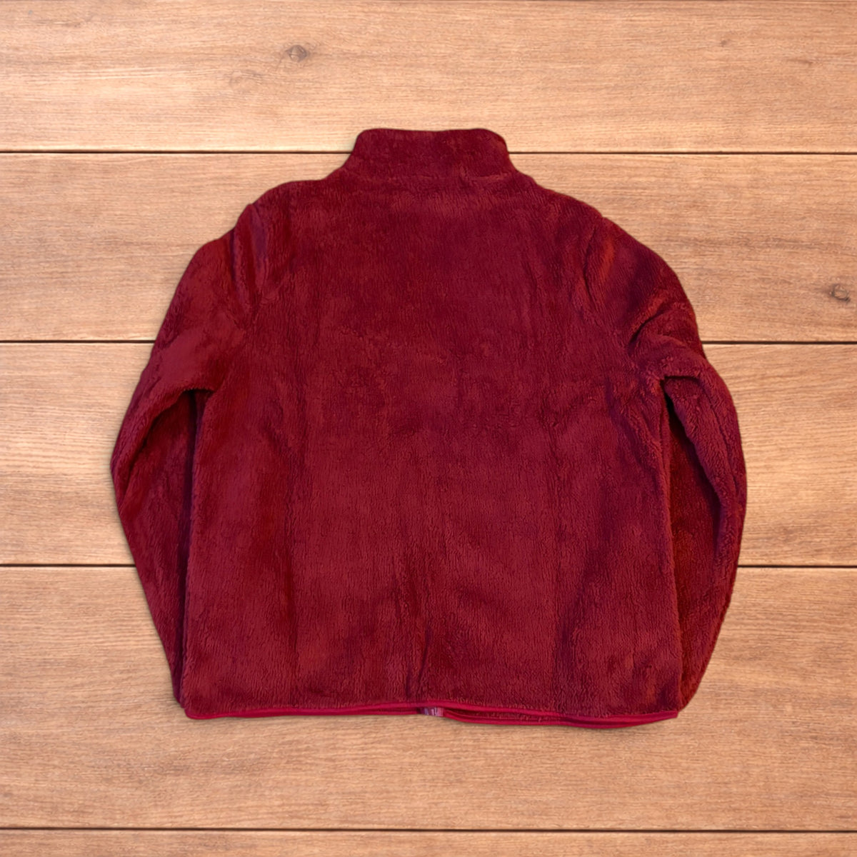 Deep dark red fluffy fleece zip up jacket laid flat on wooden surface.
