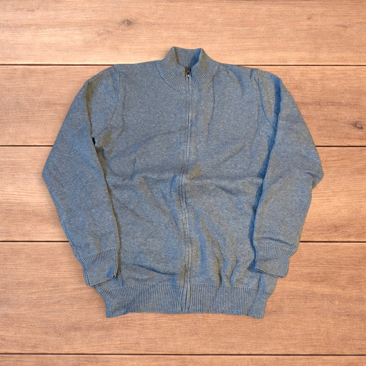 Grey vintage style knit track jacket with full zip and high neck laid flat on wooden surface.