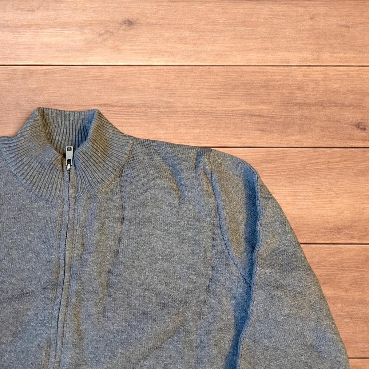 Grey vintage style knit track jacket with full zip and high neck laid flat on wooden surface.