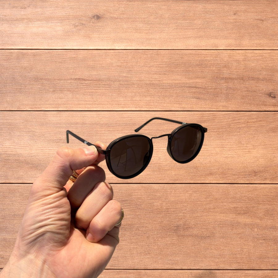 Hand holding vintage steampunk style rounded brown sunglasses with brown lenses against a wooden background