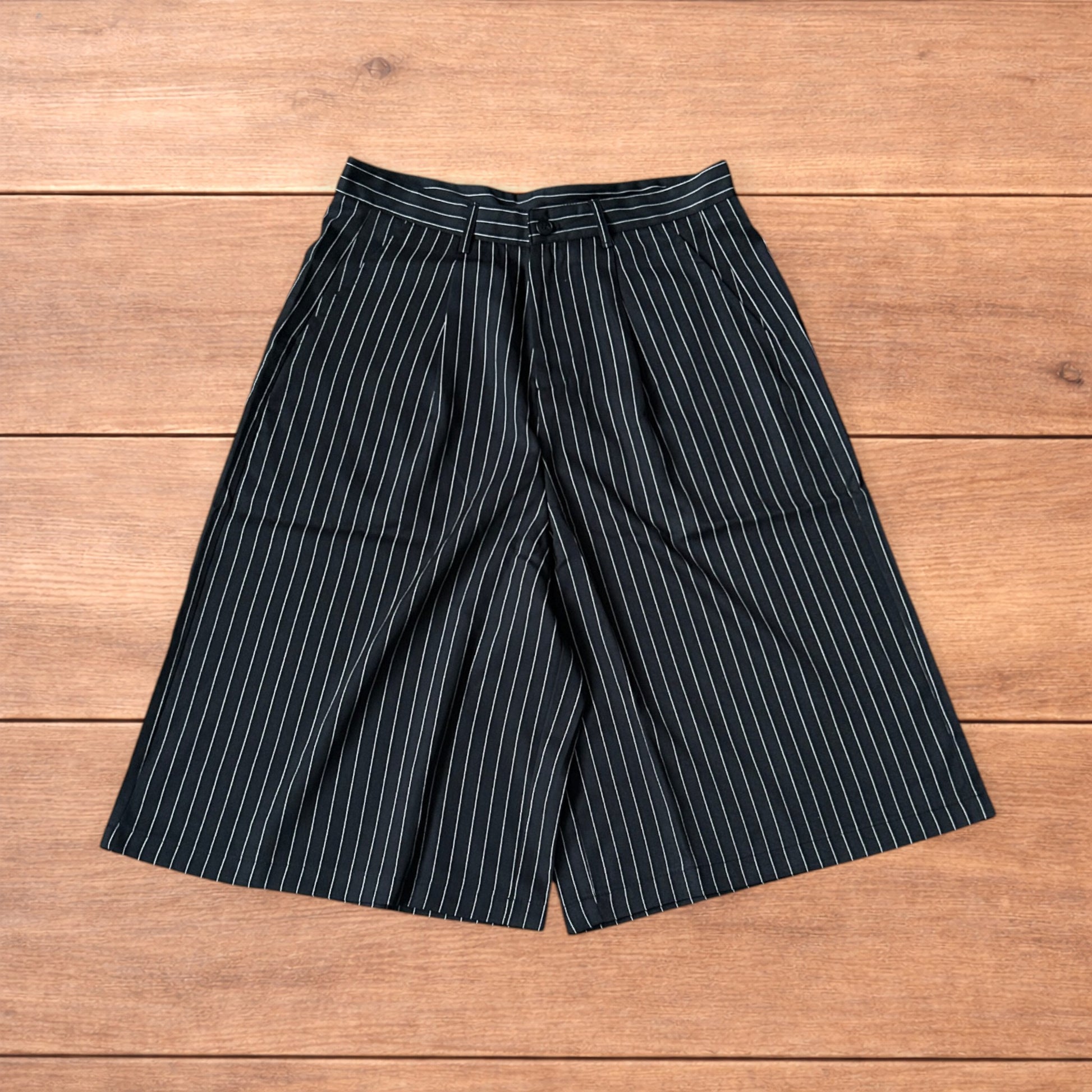 Black vintage style baggy wide long tailored shorts with white pinstripes laid flat on wooden surface